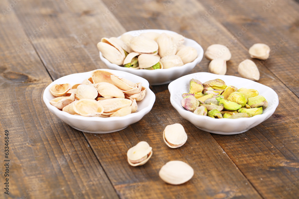 Pistachio nuts in small bowls on wooden background