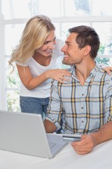 Wall Mural - Smiling young couple doing online shopping at home