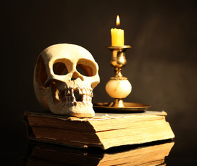 Skull and candle on old book  on dark color background