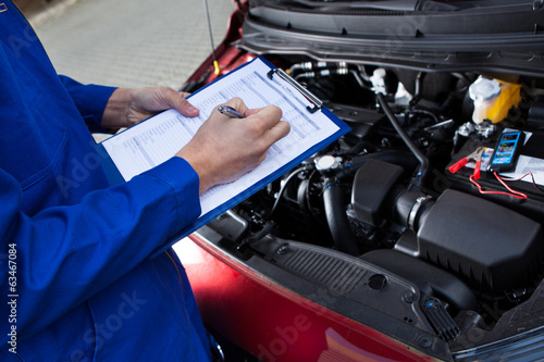 Fotografie, Obraz Mechanic Holding Clipboard In Front Of Open Car Engine