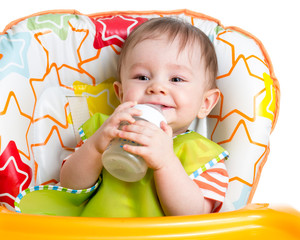 Wall Mural - smiling baby drinking from bottle sitting in high chair