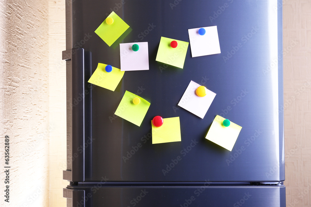 Empty paper sheets and colorful magnets on fridge door