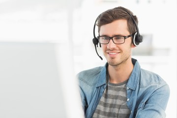 Smiling casual young man with headset using computer