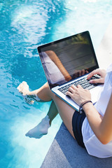 Woman working on her laptop computer sitting at poolside