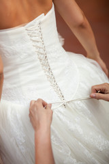 Bridesmaid helping the bride to put her wedding dress on