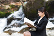 流れの急な川の近くで座って本を読むスーツの女性