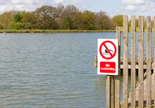 No Swimming Sign On Jetty At Edge Of Lake