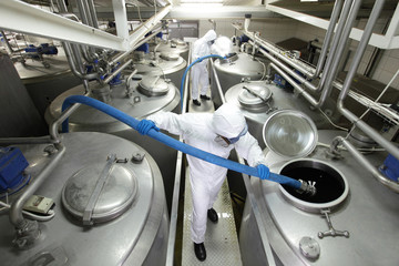 workers with blue hoses, filling large silver tanks i