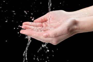 Wall Mural - Human hands with water splashing on them on black background