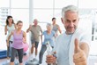 © WavebreakMediaMicro - Senior man gesturing thumbs up with people exercising in fitness