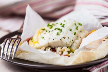 Canvas Print - White fish fillet baked in paper, parchment with rice, pepper