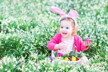 Wall Mural - Cute toddler girl in bunny ears in meadow of flowers Easter egg