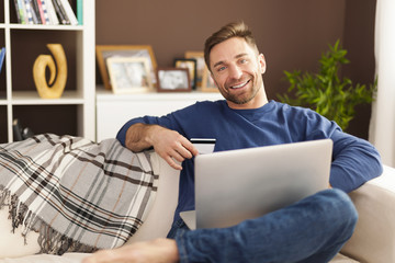 Wall Mural - Smiling man with laptop and credit card on sofa