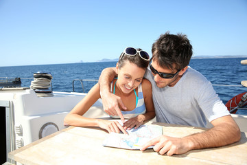 Wall Mural - Couple on a sailboat cruise looking at map