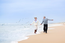 Happy Mature Couple Running At A Beautiful Winter Beach
