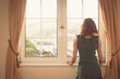 © LoloStock - Young woman in dress looking out the window