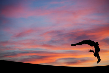 Wall Mural - silhouetted gymnast doing a back handspring in sunset sky