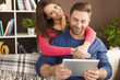 © gpointstudio - Embracing couple using digital tablet in living room