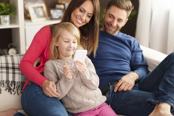 Wall Mural - Cute little girl with parents playing by mobile phone at home