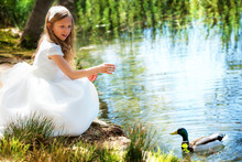 Cute Girl In White Dress Feeding A Duck.