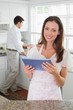 © lightwavemedia - Woman using digital tablet with man in background in kitchen