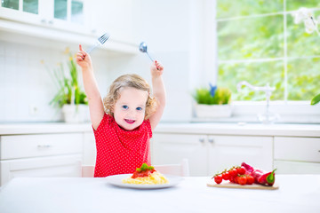 Little toddler girl eating spaghetti in a white kitchen