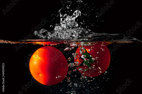 Board z aluminiowym obramowaniem Dwa pomidory wpadnięciem do wody przed czarnym tle
