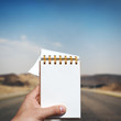 white blank notebook in man hand and empty road background