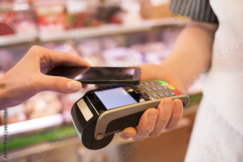 Fotografía Woman paying with NFC technology on mobile phone, in supermarket