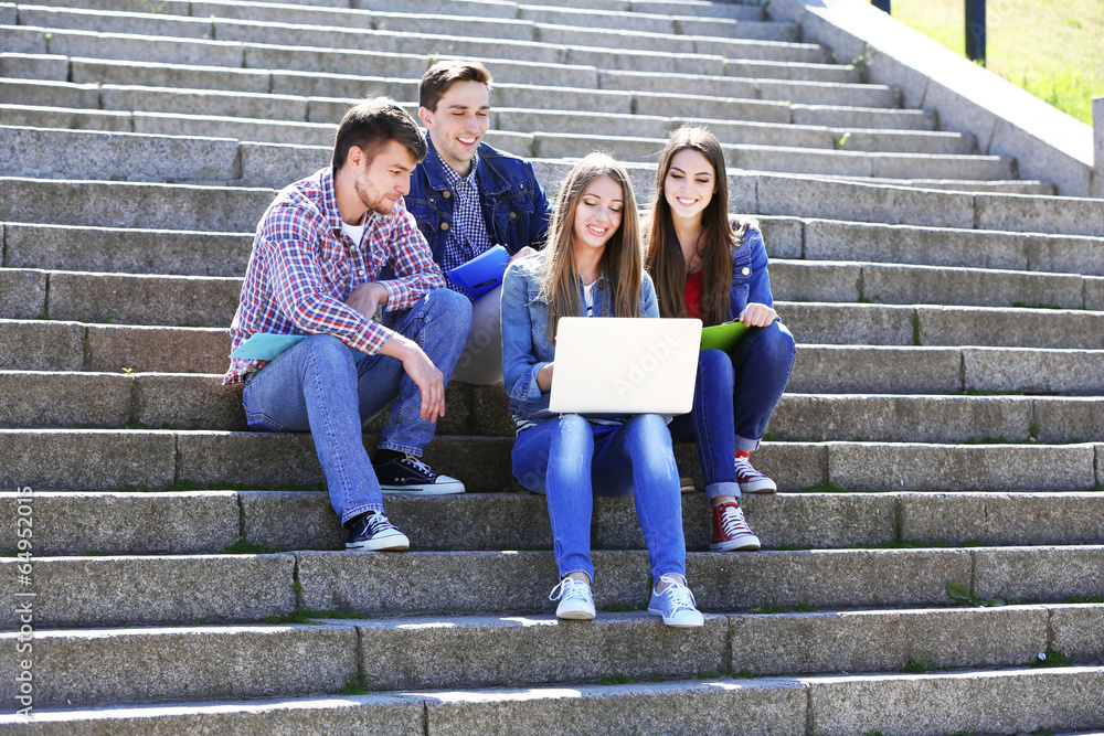 Happy students sitting on stairs in park
