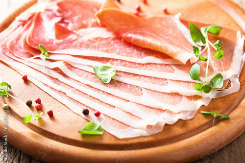 Tapeta ścienna Szynka prosciutto w plasterkach na desce do krojenia z oregano i pieprzem