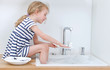 © M-Production - Happy little girl washing the dishes in the kitchen.