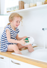 Wall Mural - Happy little girl washing the dishes in the kitchen.