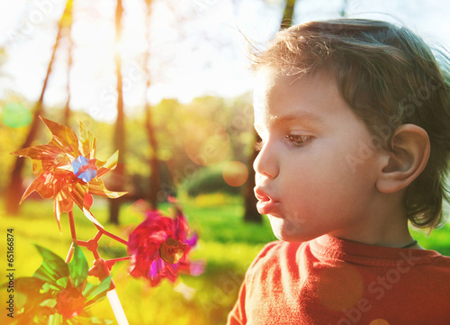 Fotografia, Obraz Portrait of a cute boy blowing wind wheel in sunshine