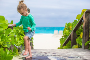 Sticker - Little cute girl washes out the sand from her feet on tropical