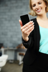 Canvas Print - Happy woman holding smartphone in office. Focus on smartphone