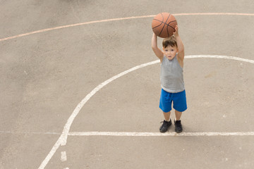 Wall Mural - Cute little boy practising on a basketball court