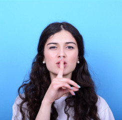 Portrait of girl with gesture for silence against blue backgroun