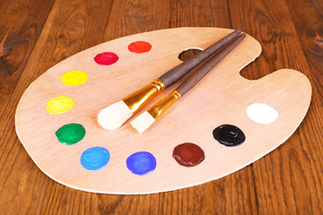 Canvas Print - Wooden art palette with paint and brushes on table close-up