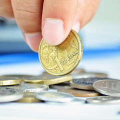 Fingers picking up a coin - one Australian dollar (AUD)