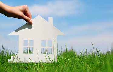 Paper house in green grass over blue sky. Concept