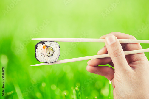 Naklejka samoprzylepna Ręka trzyma sushi roll za pomocą pałeczki