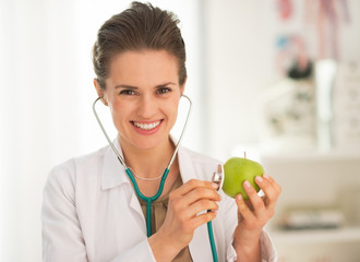 Wall Mural - Happy medical doctor woman examining apple with stethoscope