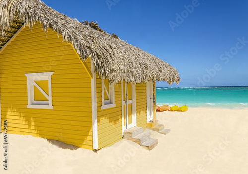 Photographie Wooden yellow hut on the beach covered with thatch and kayaks