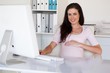 © WavebreakMediaMicro - Casual pregnant businesswoman touching her bump at her desk smil