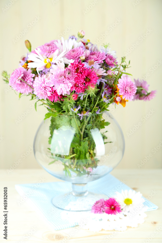 Wildflowers in glass vase on table on light background
