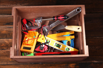 Wooden box with different tools, on rustic wooden background