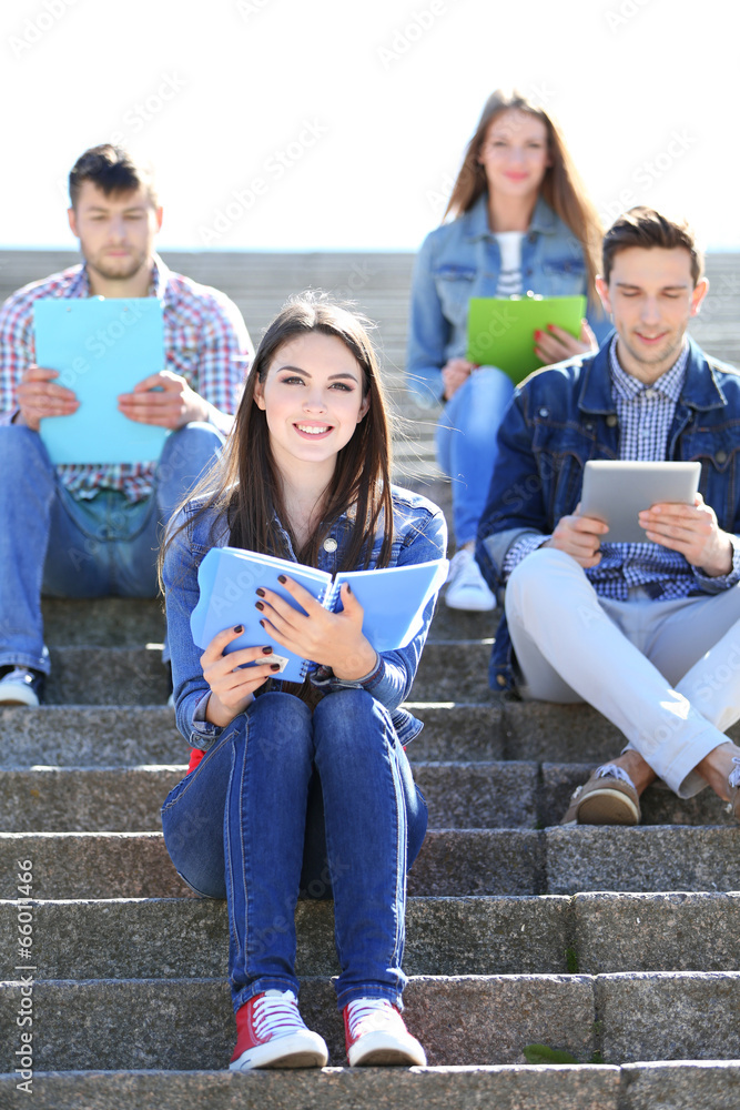 Happy students sitting on stairs in park