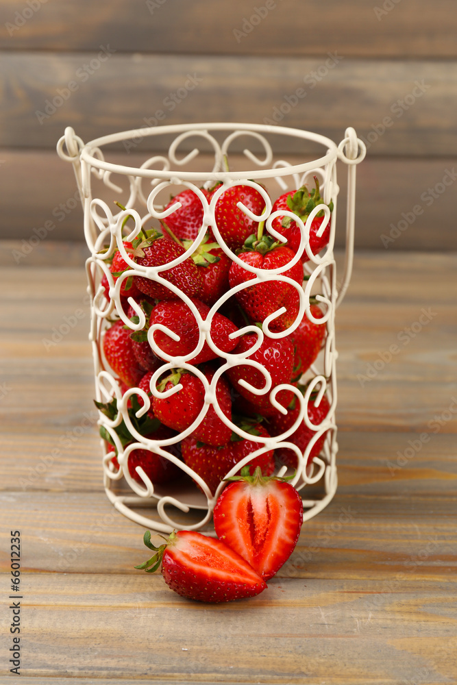 Red ripe strawberries in decorative vase on wooden background