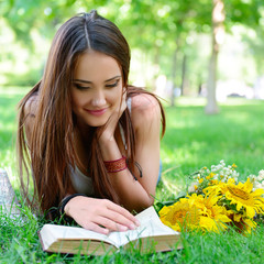 beautiful cheerful girl reading book in the summer park